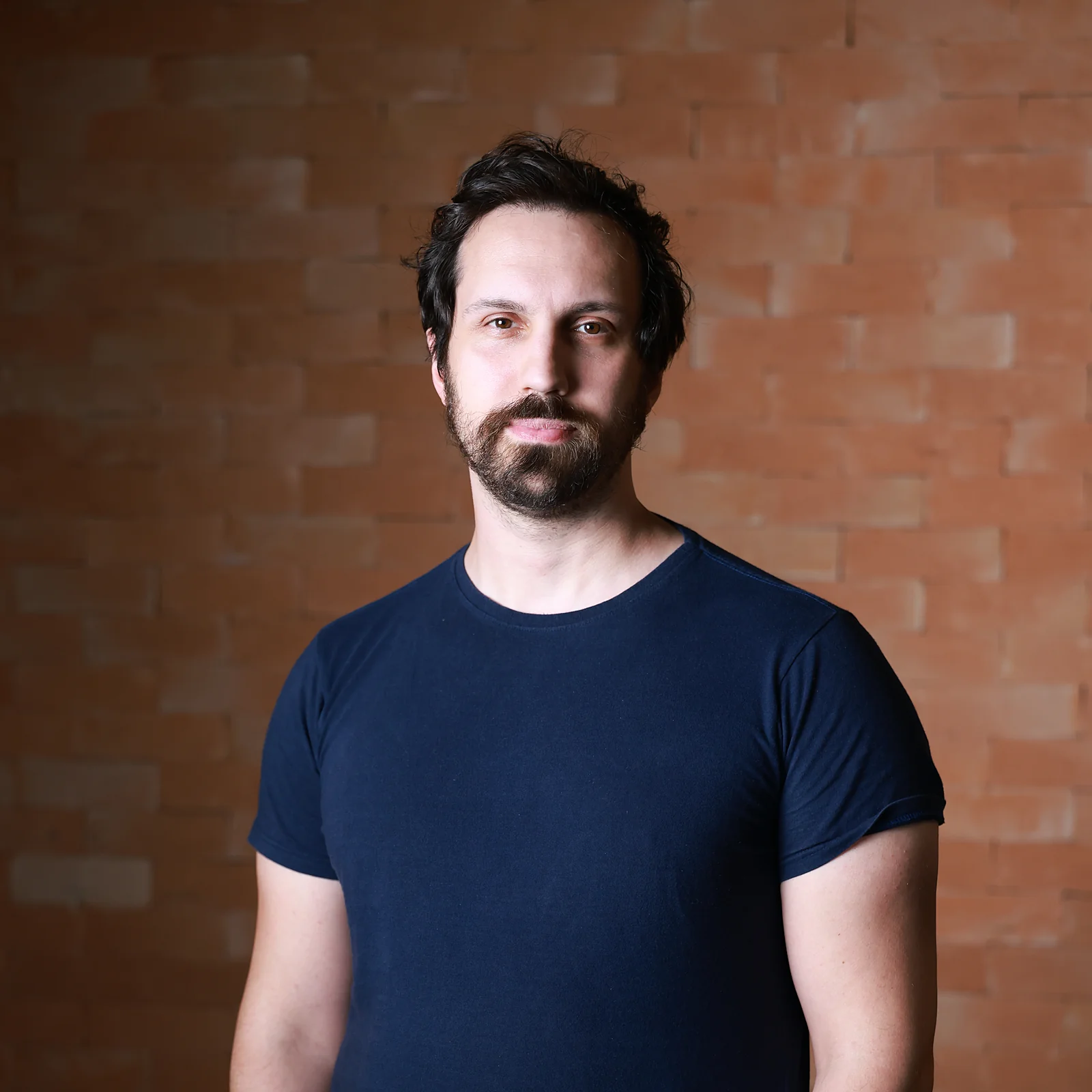 Felipe Fiori, psychoanalyst, looking at the camera in front of a brick wall, one hand in his pocket.